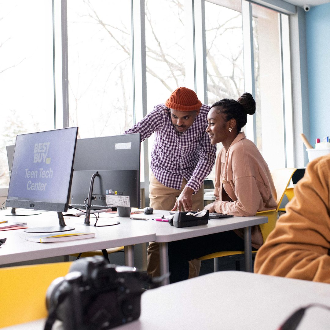 Mentor and teen sit at a computer and discuss what's on screen (not visible)