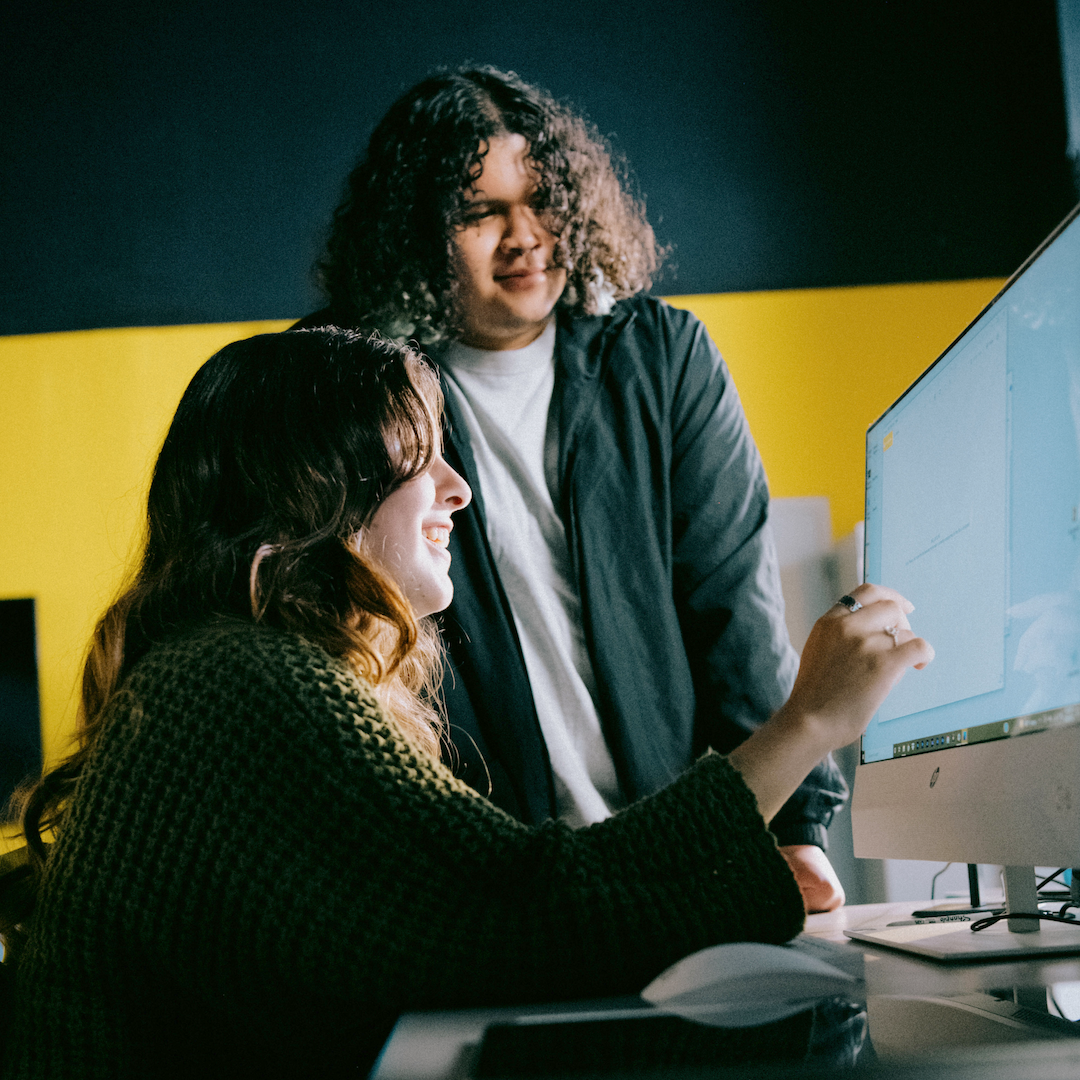 two teens talking as they stare at a computer together